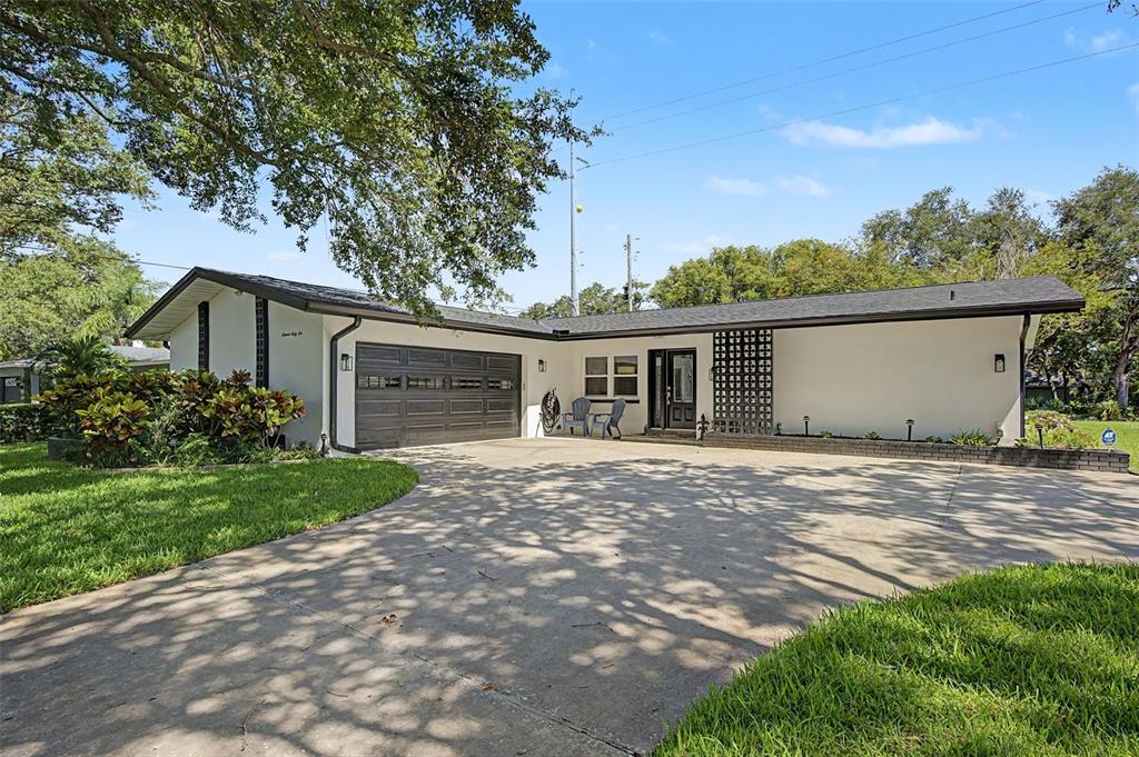 A single-story house with a white exterior, a dark garage door, and a concrete driveway — 1666 SOUVENIR DRIVE, CLEARWATER, FL