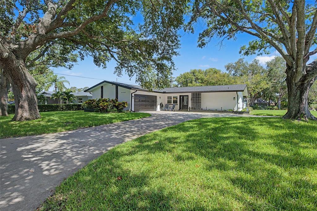A single-story white house with a dark roof and garage sits behind a large lawn — 1666 SOUVENIR DRIVE, CLEARWATER, FL