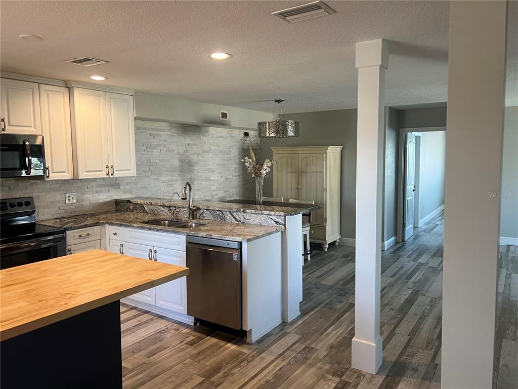 A kitchen with white cabinets, granite countertops, and a wood-topped island overlooks a dining area — 8211 BRENT STREET UNIT 828, PORT RICHEY, FL
