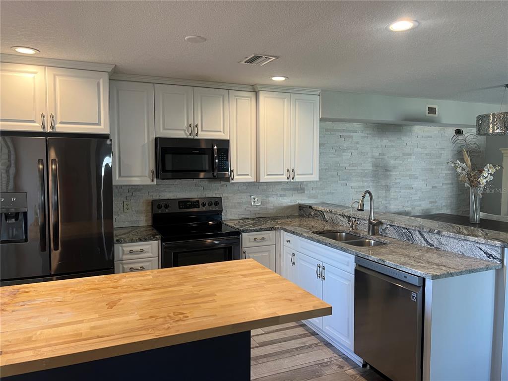 A kitchen features white cabinets, granite countertops, a butcher block island, and stainless steel appliances — 8211 BRENT STREET UNIT 828, PORT RICHEY, FL