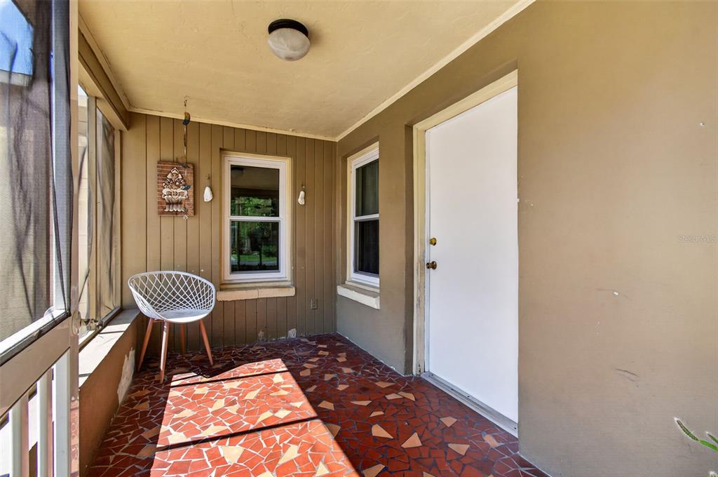 A covered porch features a mosaic tile floor, a white chair, and a white door — 715 NW 22ND AVENUE, GAINESVILLE, FL