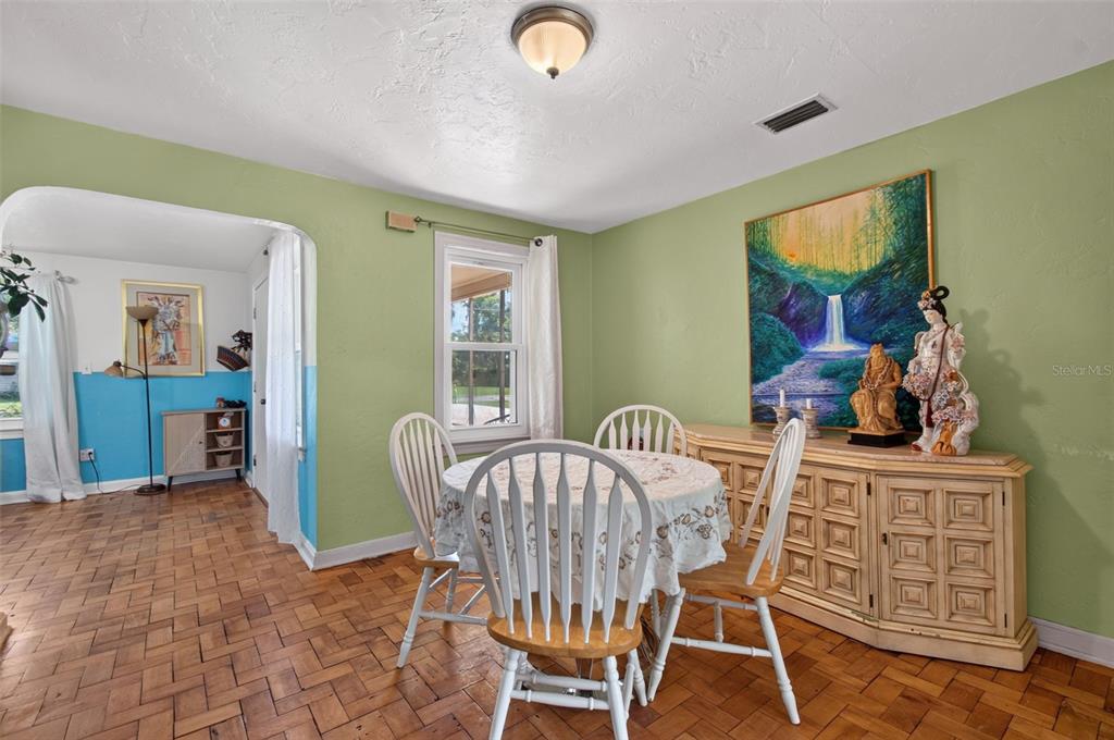 A dining room features green walls, a round table with white chairs, and parquet flooring — 715 NW 22ND AVENUE, GAINESVILLE, FL