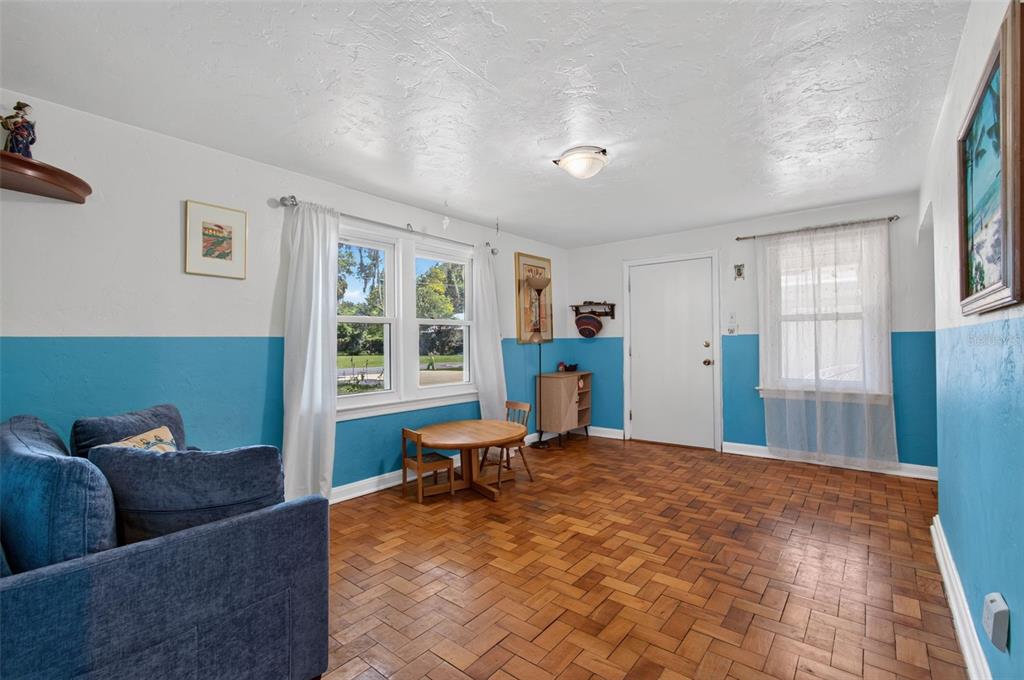 A living room with blue wainscoting, parquet wood flooring, a small wooden table, and windows — 715 NW 22ND AVENUE, GAINESVILLE, FL