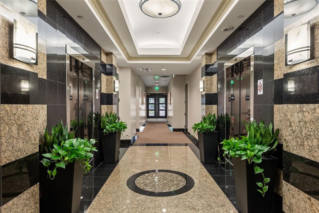 A hallway with two elevators, marble floors, potted plants, and wall sconces in a building — 1525 INTERNATIONAL PARKWAY UNIT 4071, LAKE MARY, FL