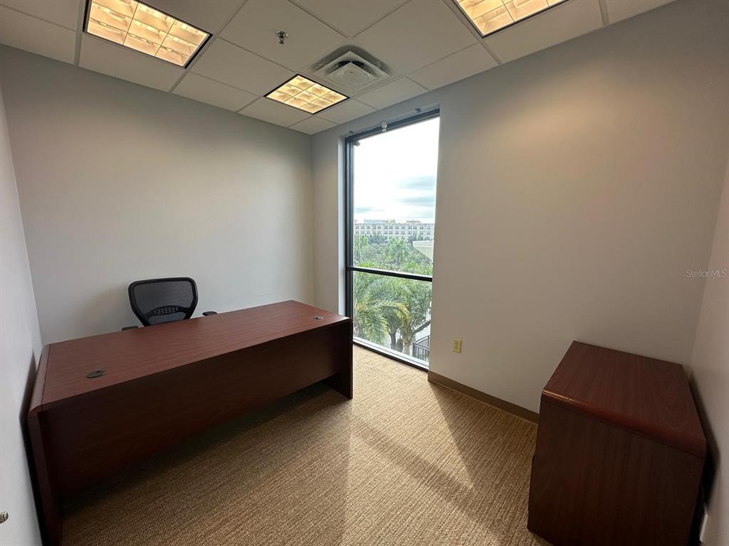 An office features a dark wood desk, a rolling chair, beige carpet, and a large window — 1525 INTERNATIONAL PARKWAY UNIT 4071, LAKE MARY, FL