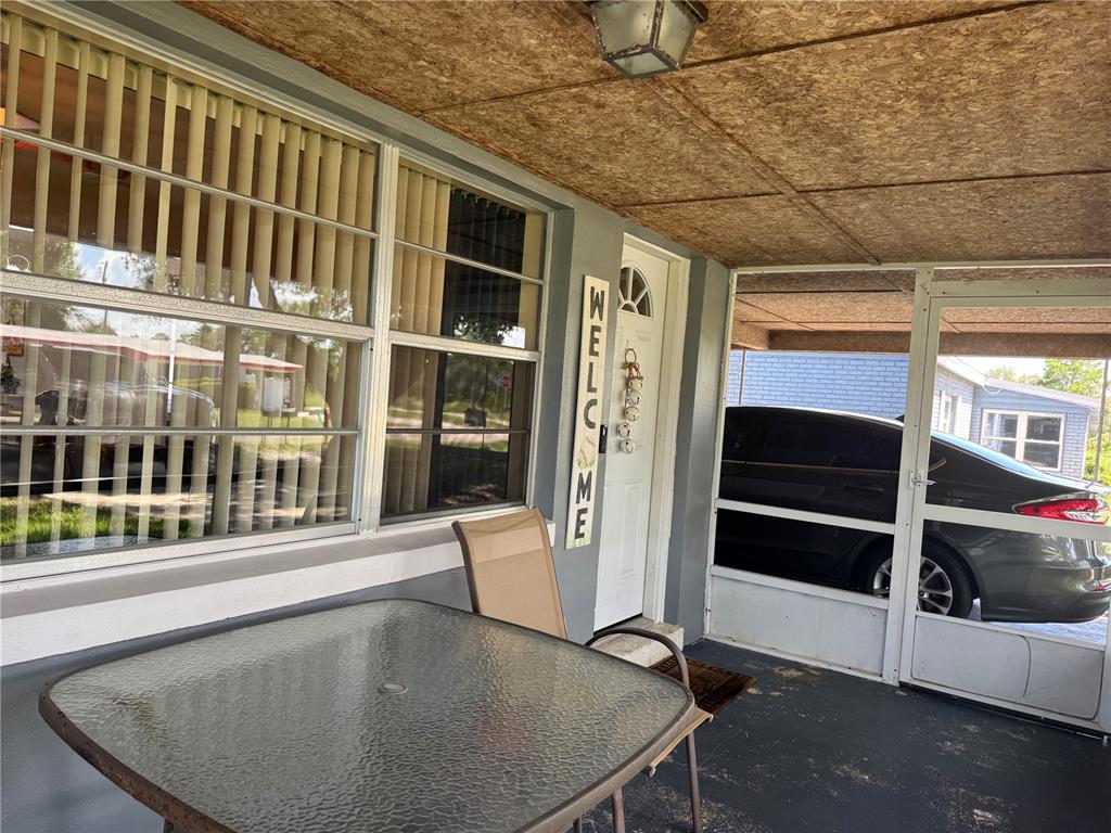 A covered porch features a glass-topped table, a chair, and a white door with signage — 519 THOMAS AVENUE, FROSTPROOF, FL