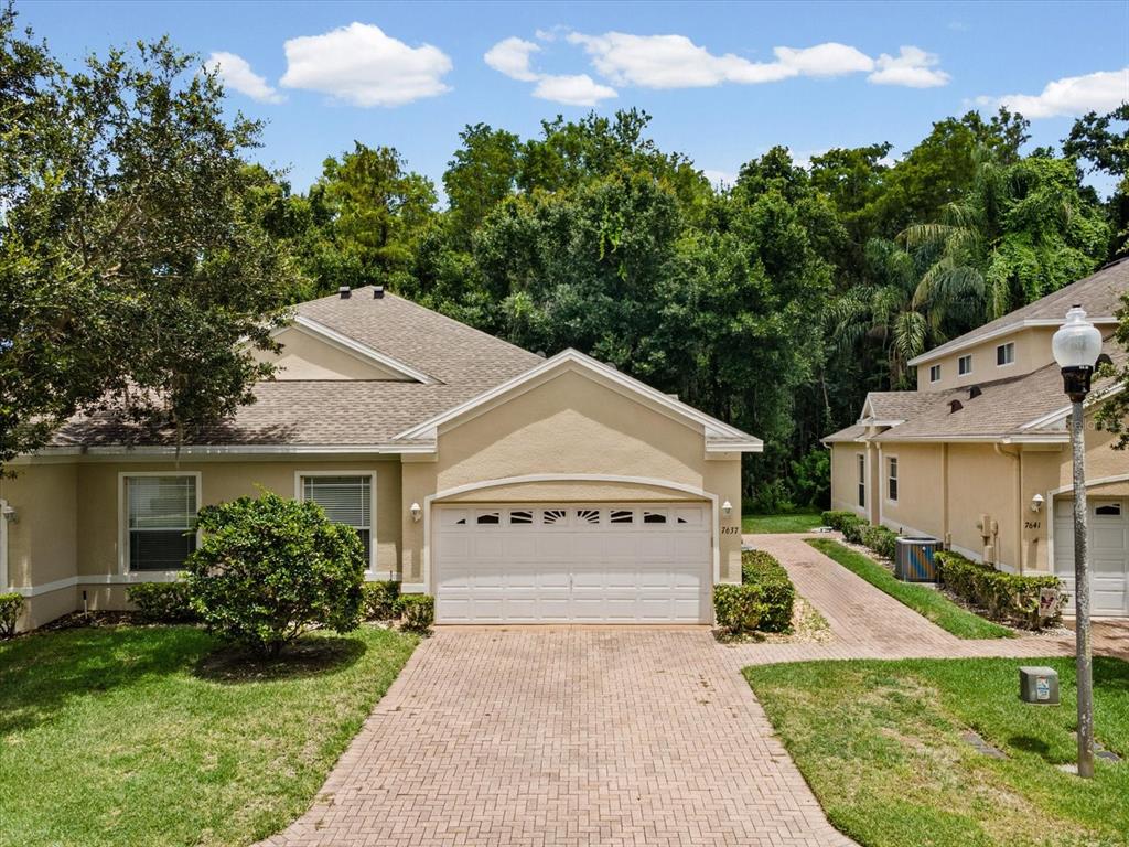 A tan-colored townhouse with a white garage door and a brick paver driveway — 7637 WIMPOLE DRIVE, NEW PORT RICHEY, FL