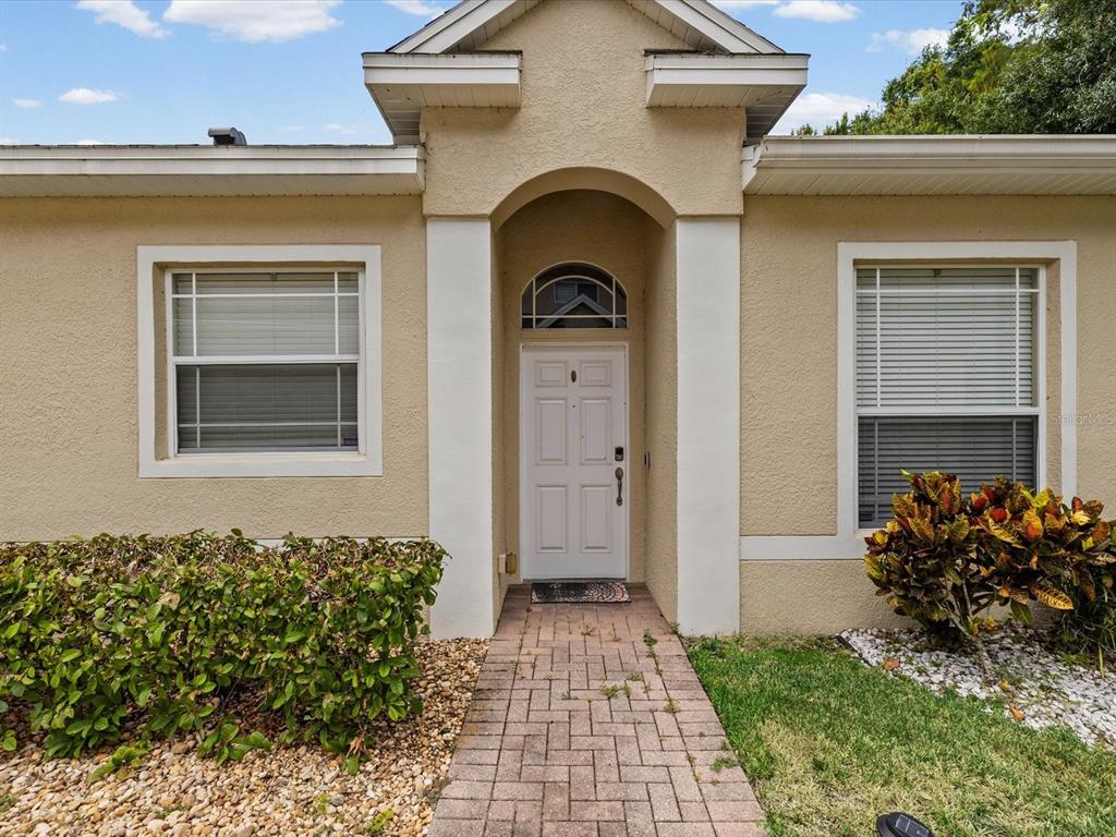The front exterior of a tan house features a brick walkway leading to the entrance — 7637 WIMPOLE DRIVE, NEW PORT RICHEY, FL