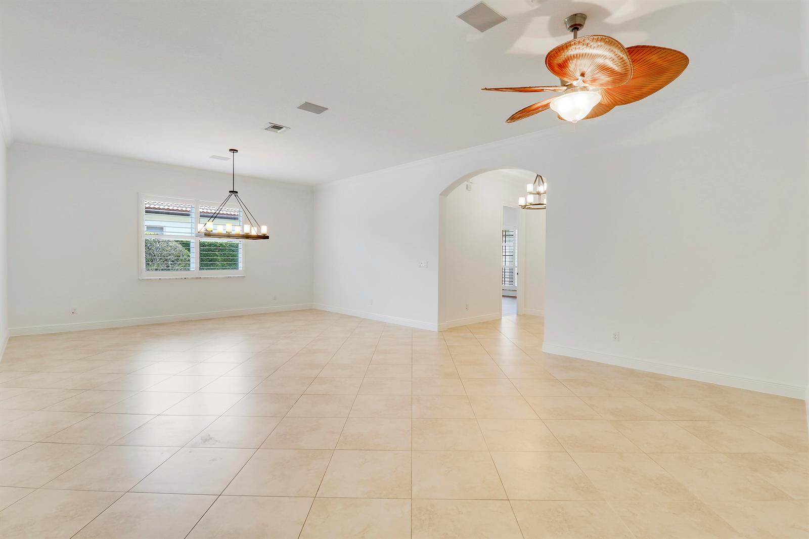 A spacious, empty room features light-colored tile flooring, a ceiling fan, and a chandelier — 119 Steeple Circle, Jupiter FL 33458, JUPITER, FL