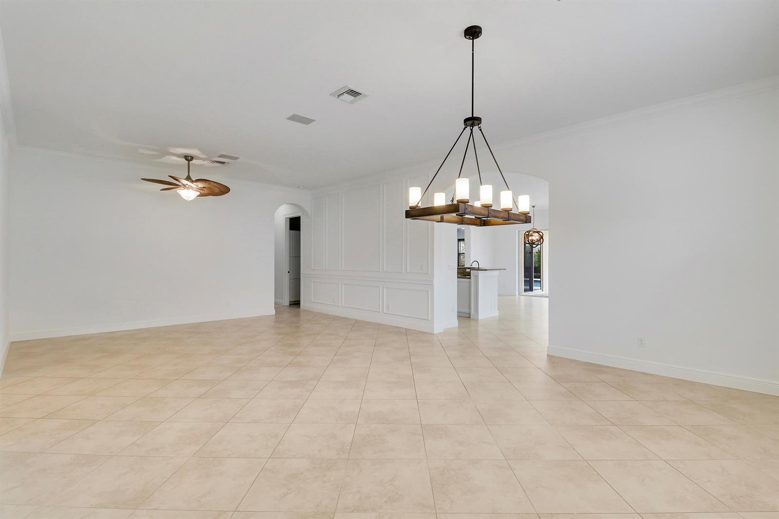 A spacious, empty room features light-colored tile floors, a chandelier, and a ceiling fan — 119 Steeple Circle, Jupiter FL 33458, JUPITER, FL