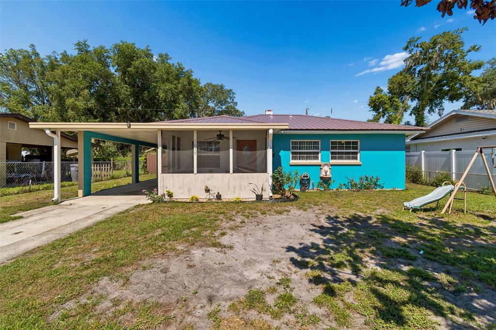 A turquoise single-story house features a metal roof, a screened-in porch, and a carport — 1038 CANAL DRIVE W, LAKELAND, FL