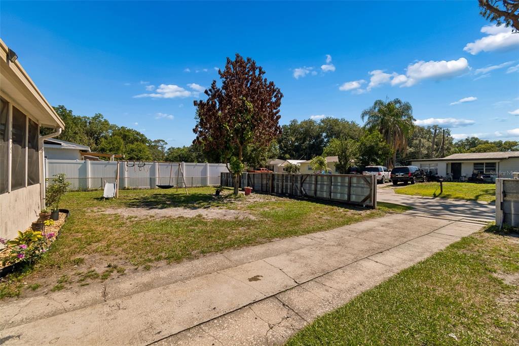 A grassy backyard features a swing set, a central tree, and a concrete driveway — 1038 CANAL DRIVE W, LAKELAND, FL