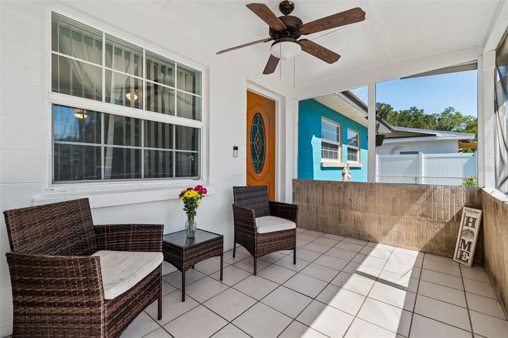 A covered porch features tiled flooring, two wicker chairs, a small table, and a ceiling fan — 1038 CANAL DRIVE W, LAKELAND, FL