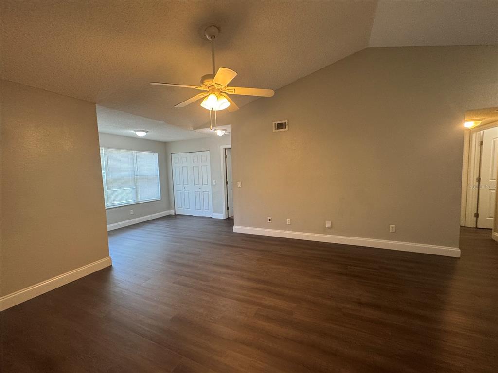 An empty living room features dark wood-look flooring, light gray walls, and a ceiling fan — 4532 COMMANDER DRIVE UNIT 2131, ORLANDO, FL