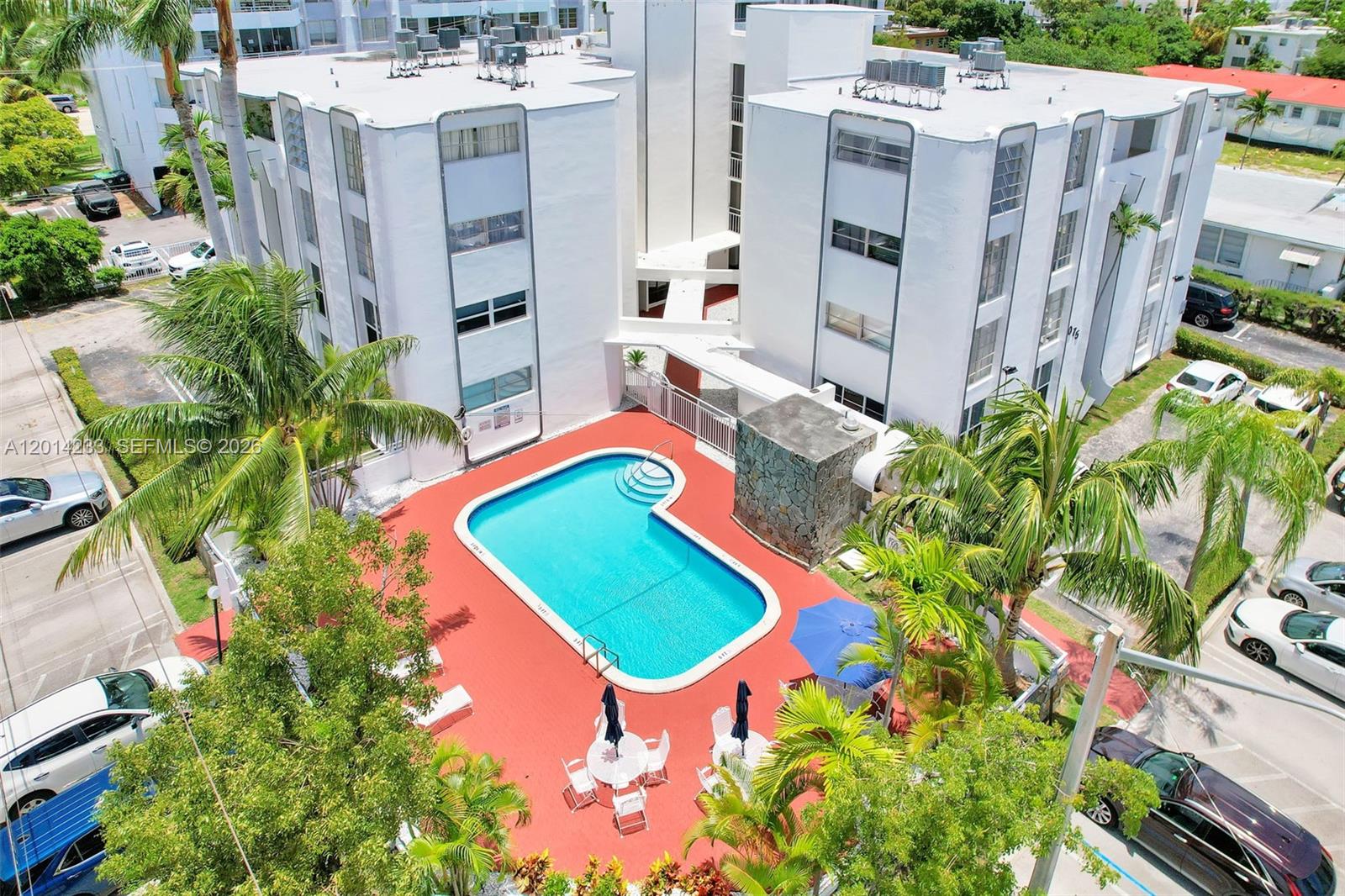 An aerial view shows a swimming pool with a red deck between two white buildings — 1075 93rd St # 207, Bay Harbor Islands FL 33154, BAY HARBOR ISLANDS, FL
