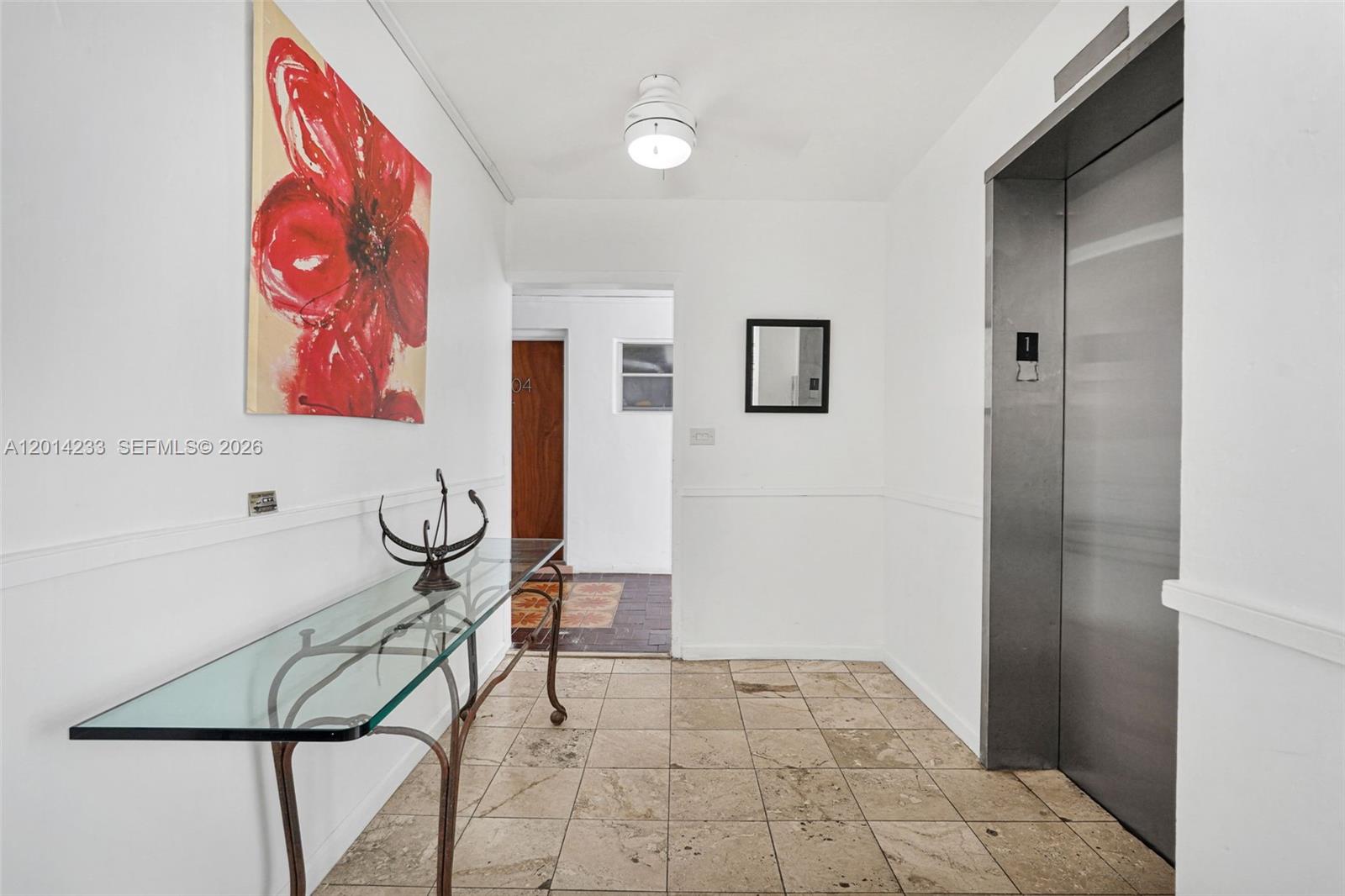 A hallway features a glass console table, a red floral painting, and a metal elevator — 1075 93rd St # 207, Bay Harbor Islands FL 33154, BAY HARBOR ISLANDS, FL