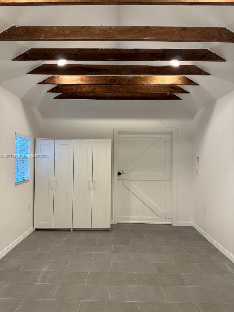 A room with gray tile flooring, white walls, a barn-style door, and exposed wooden ceiling beams — 3113 SW 14th St # A, Miami FL 33145, MIAMI, FL