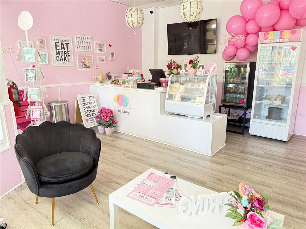 A bright bakery interior features a service counter, display cases, pink walls, and seating — 4127 NW 16TH BOULEVARD, GAINESVILLE, FL