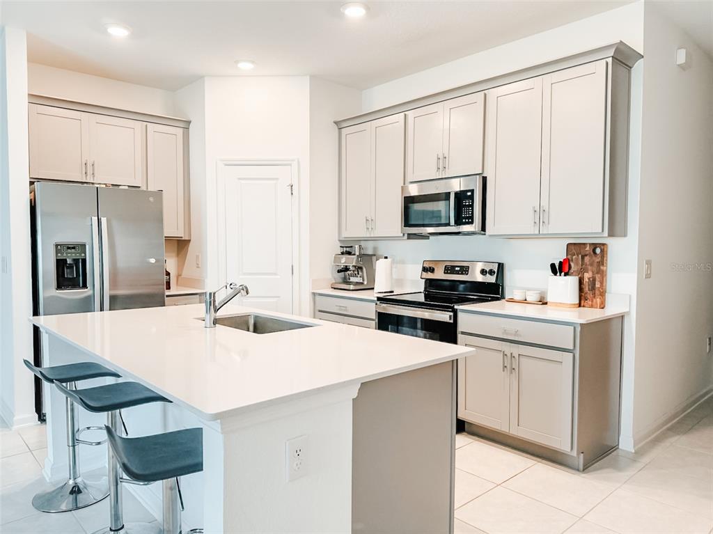 A kitchen features light gray cabinets, stainless steel appliances, and a white quartz island — 1828 PERCH HAMMOCK LOOP, GROVELAND, FL