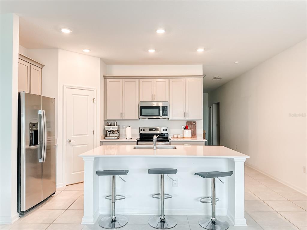A kitchen features a white island with three bar stools, stainless appliances, and light cabinetry — 1828 PERCH HAMMOCK LOOP, GROVELAND, FL