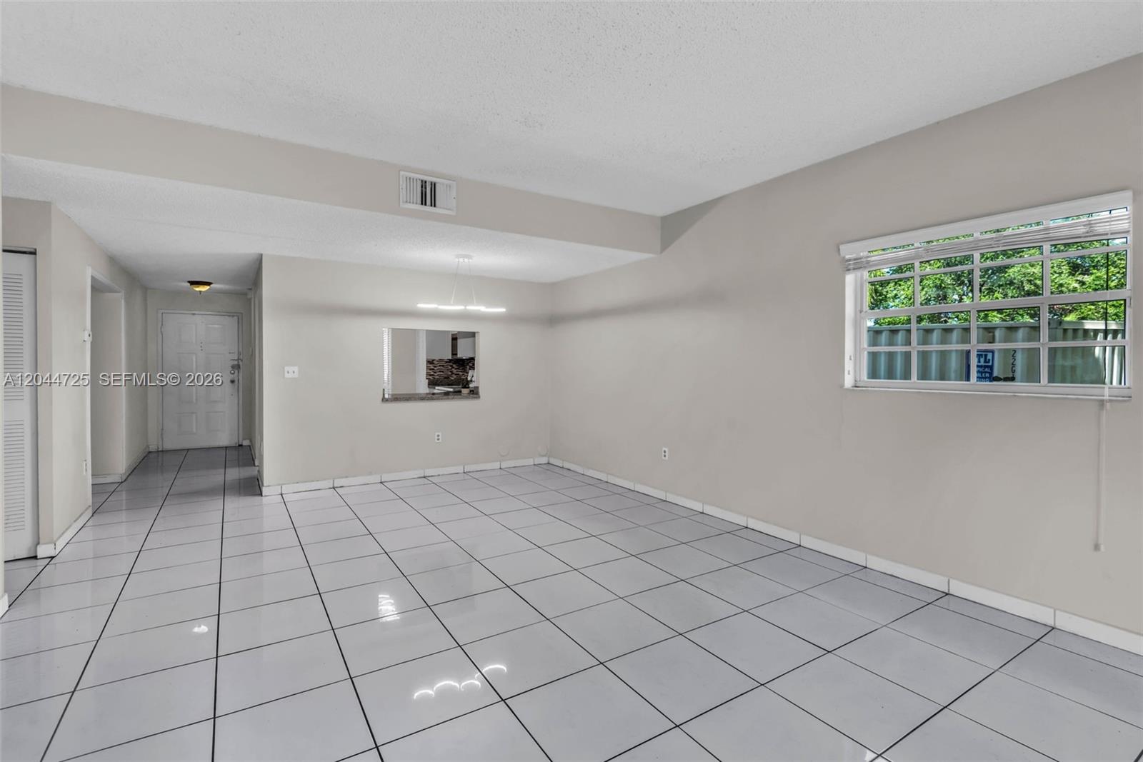 An empty room features white tile flooring, light-colored walls, a window, and a pass-through opening — 10018 Hammocks Blvd # 5, Miami FL 33196, MIAMI, FL