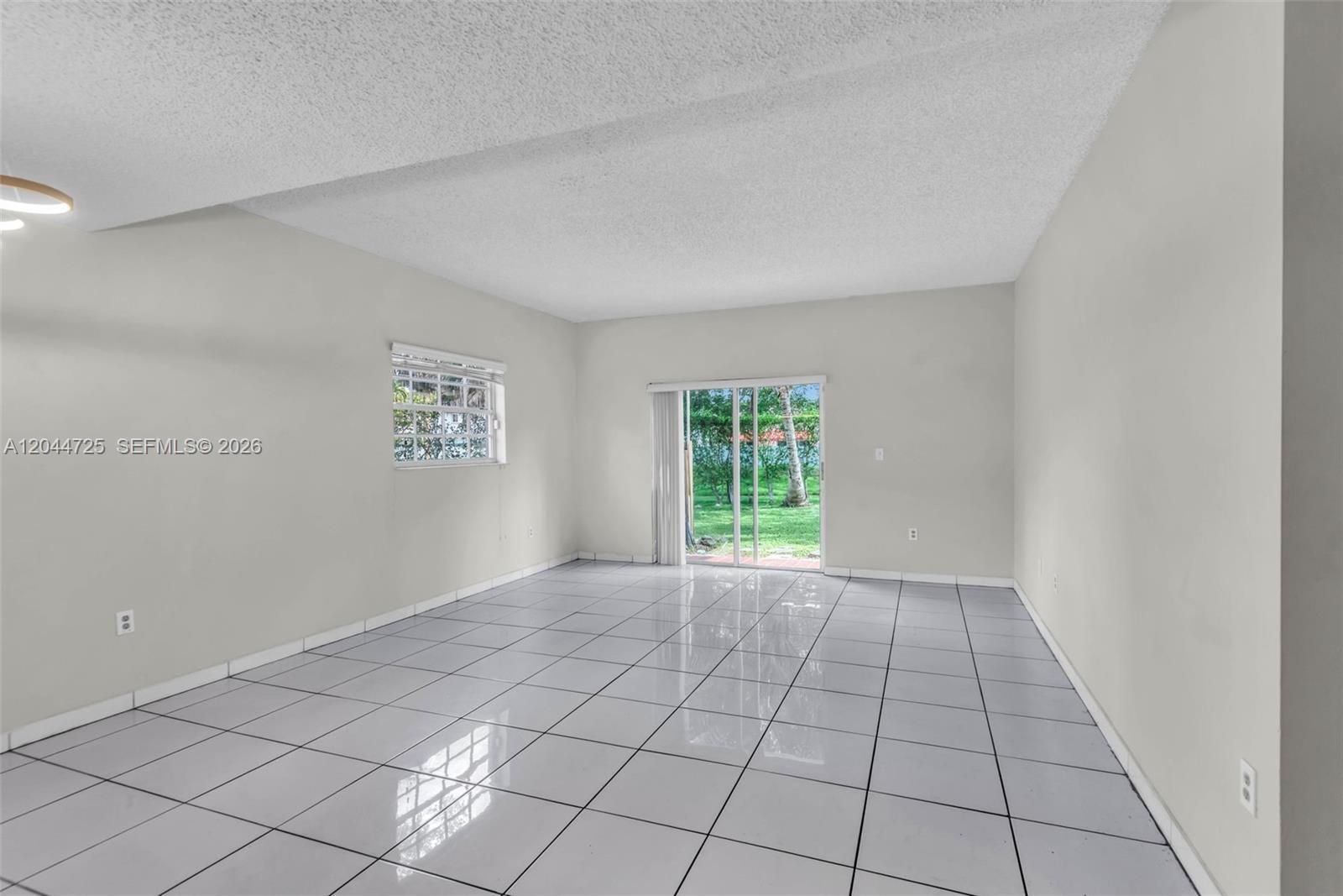 This empty room features white tiled floors, a textured ceiling, and a sliding glass door — 10018 Hammocks Blvd # 5, Miami FL 33196, MIAMI, FL