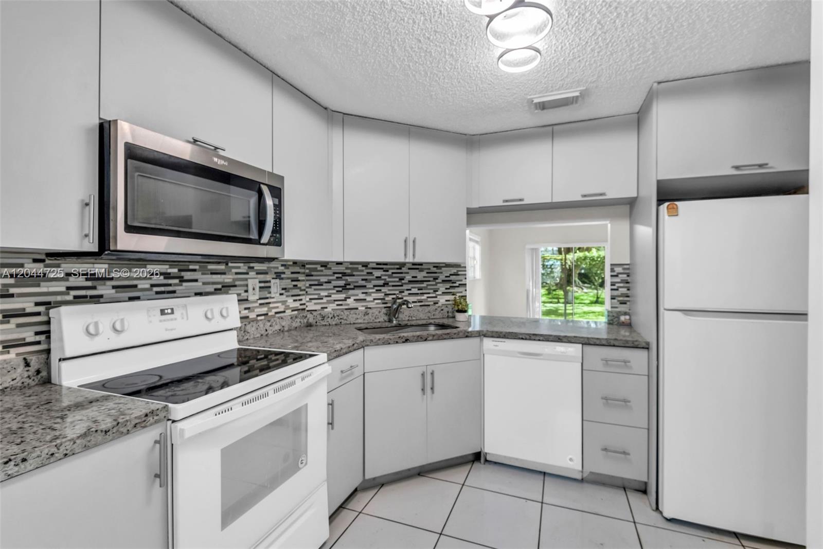 A kitchen features white cabinets, granite countertops, a tiled backsplash, and white appliances — 10018 Hammocks Blvd # 5, Miami FL 33196, MIAMI, FL