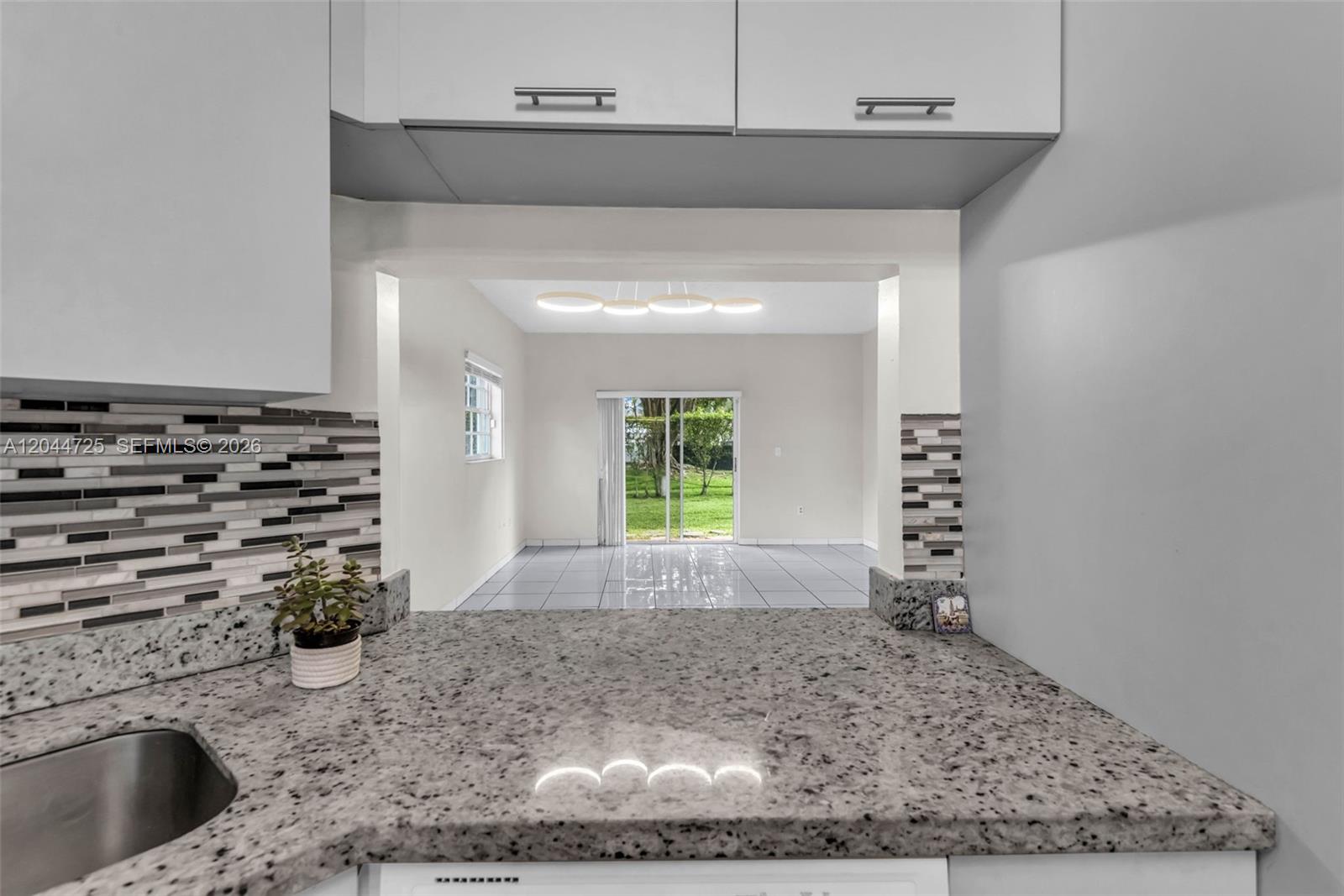 A kitchen pass-through overlooks a living area with tile floors and sliding glass doors — 10018 Hammocks Blvd # 5, Miami FL 33196, MIAMI, FL