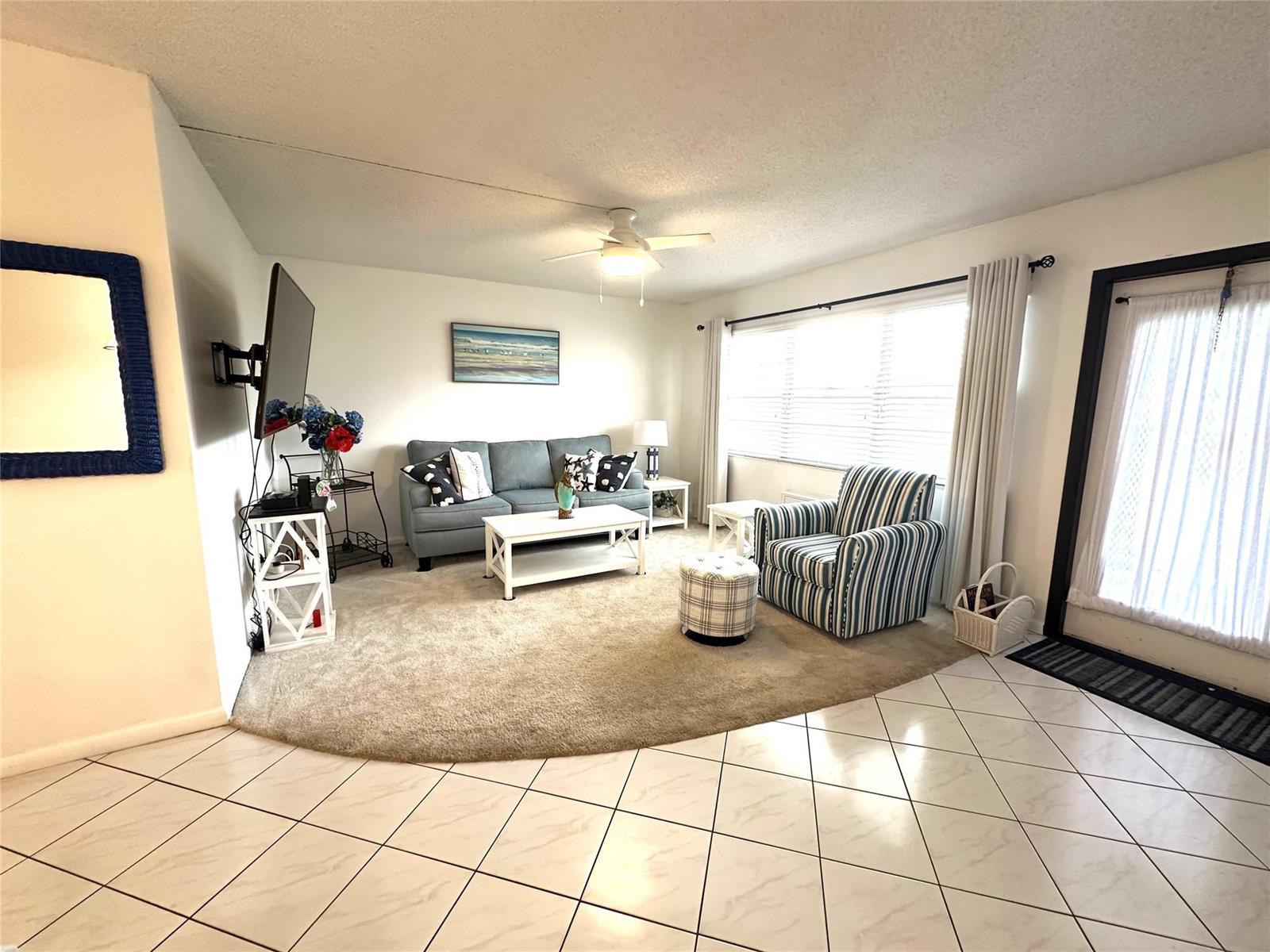 A living room features a circular carpet, a blue sofa, a striped armchair, and tile flooring — 131 Oakridge J # 131, Deerfield Beach FL 33442, DEERFIELD BEACH, FL