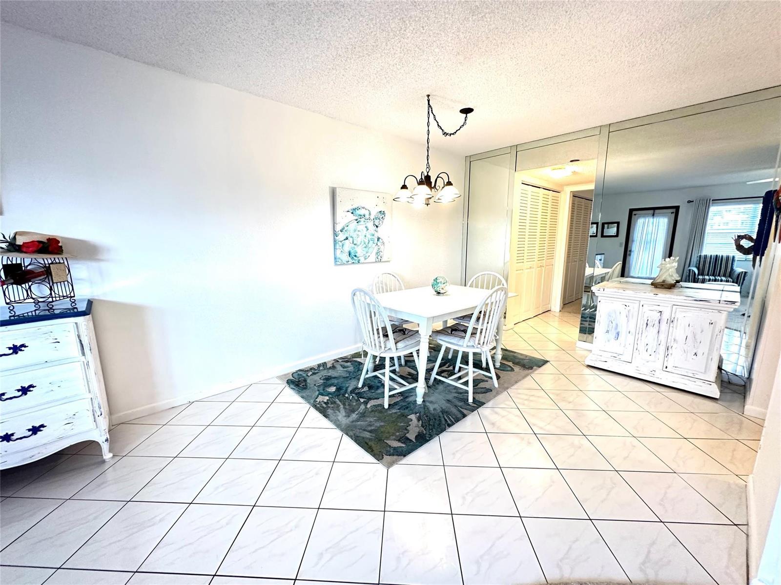 A dining area features a white table, four chairs, a patterned rug, and mirrored walls — 131 Oakridge J # 131, Deerfield Beach FL 33442, DEERFIELD BEACH, FL