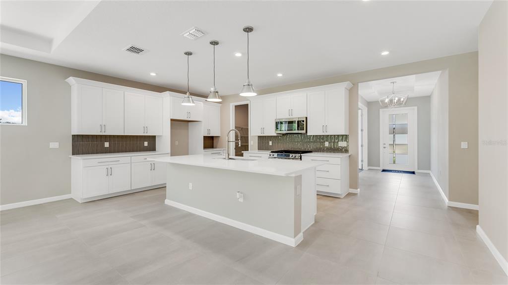 A modern kitchen features white cabinetry, a central island, stainless steel appliances, and tile flooring — 1213 CRESSWIND BOULEVARD, DELAND, FL