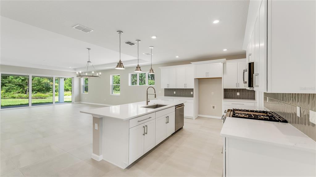 A modern kitchen features white cabinetry, a large center island, and an open living area — 1213 CRESSWIND BOULEVARD, DELAND, FL