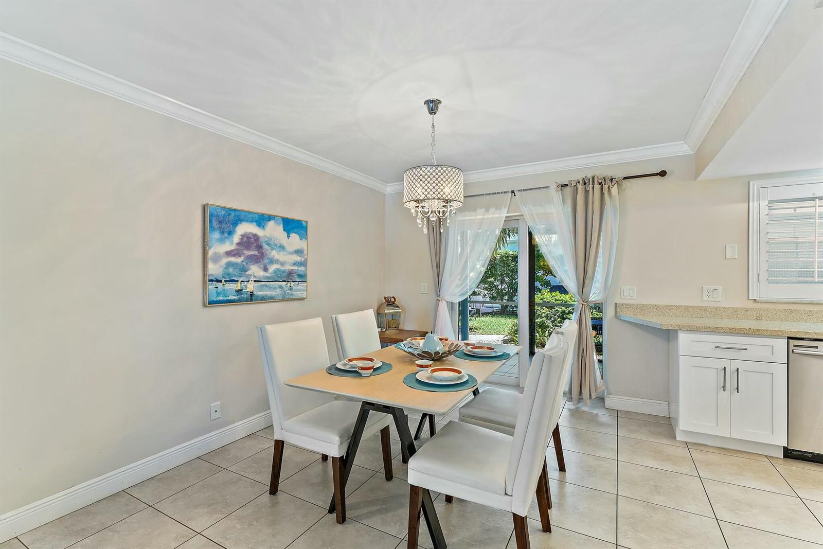 A dining area features a light-wood table, white chairs, a crystal chandelier, and tile flooring — 3036 Park Avenue, Riviera Beach FL 33404, RIVIERA BEACH, FL