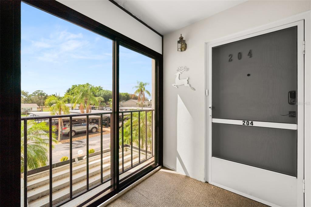A covered balcony features a screen door, a metal railing, and a view of parking — 117 COUNTRY CLUB DRIVE UNIT 204, LAKE PLACID, FL