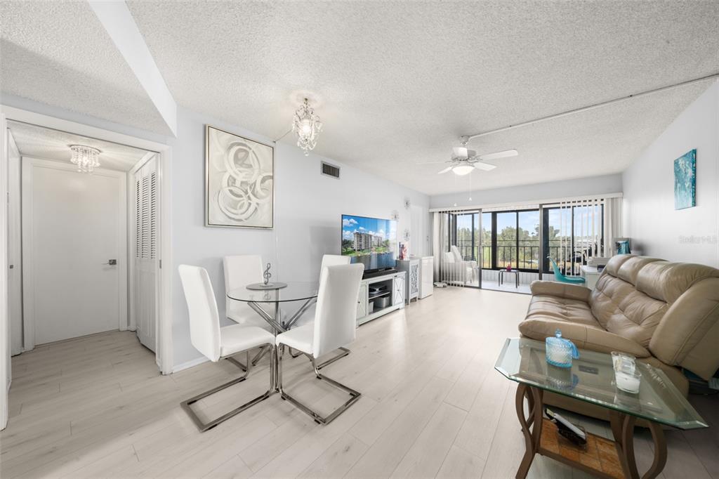 A living and dining area with light wood floors, white furniture, and a glass balcony door — 117 COUNTRY CLUB DRIVE UNIT 204, LAKE PLACID, FL