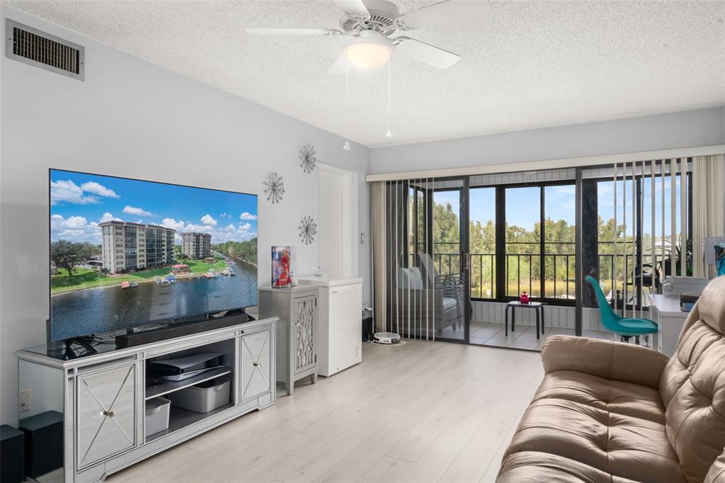 A living room with light wood flooring, a large television, and a balcony overlooking water — 117 COUNTRY CLUB DRIVE UNIT 204, LAKE PLACID, FL