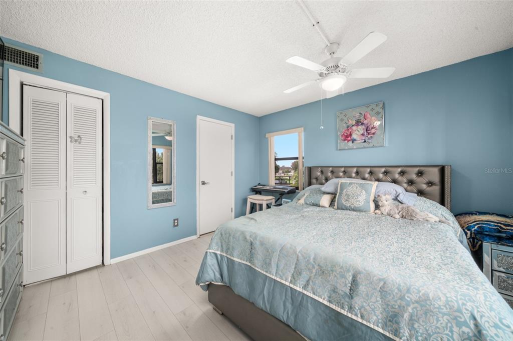 A bedroom with light blue walls, white flooring, a ceiling fan, and a tufted headboard — 117 COUNTRY CLUB DRIVE UNIT 204, LAKE PLACID, FL
