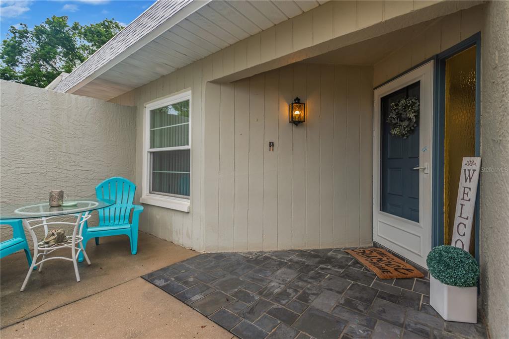 A covered front porch features a dark tiled entryway, a blue door, and patio furniture — 3943 TROPHY BOULEVARD UNIT 4604, NEW PORT RICHEY, FL