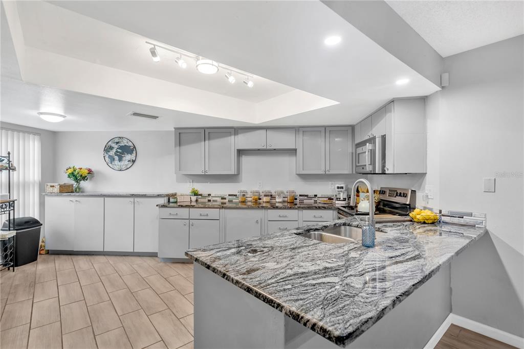 A kitchen features gray cabinetry, granite countertops, a breakfast bar, and light-colored tile flooring — 3943 TROPHY BOULEVARD UNIT 4604, NEW PORT RICHEY, FL