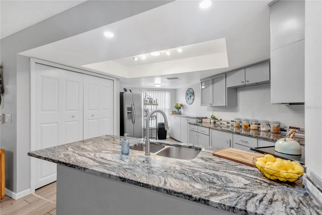 A kitchen features a granite-topped island, grey cabinetry, and a recessed ceiling light fixture — 3943 TROPHY BOULEVARD UNIT 4604, NEW PORT RICHEY, FL