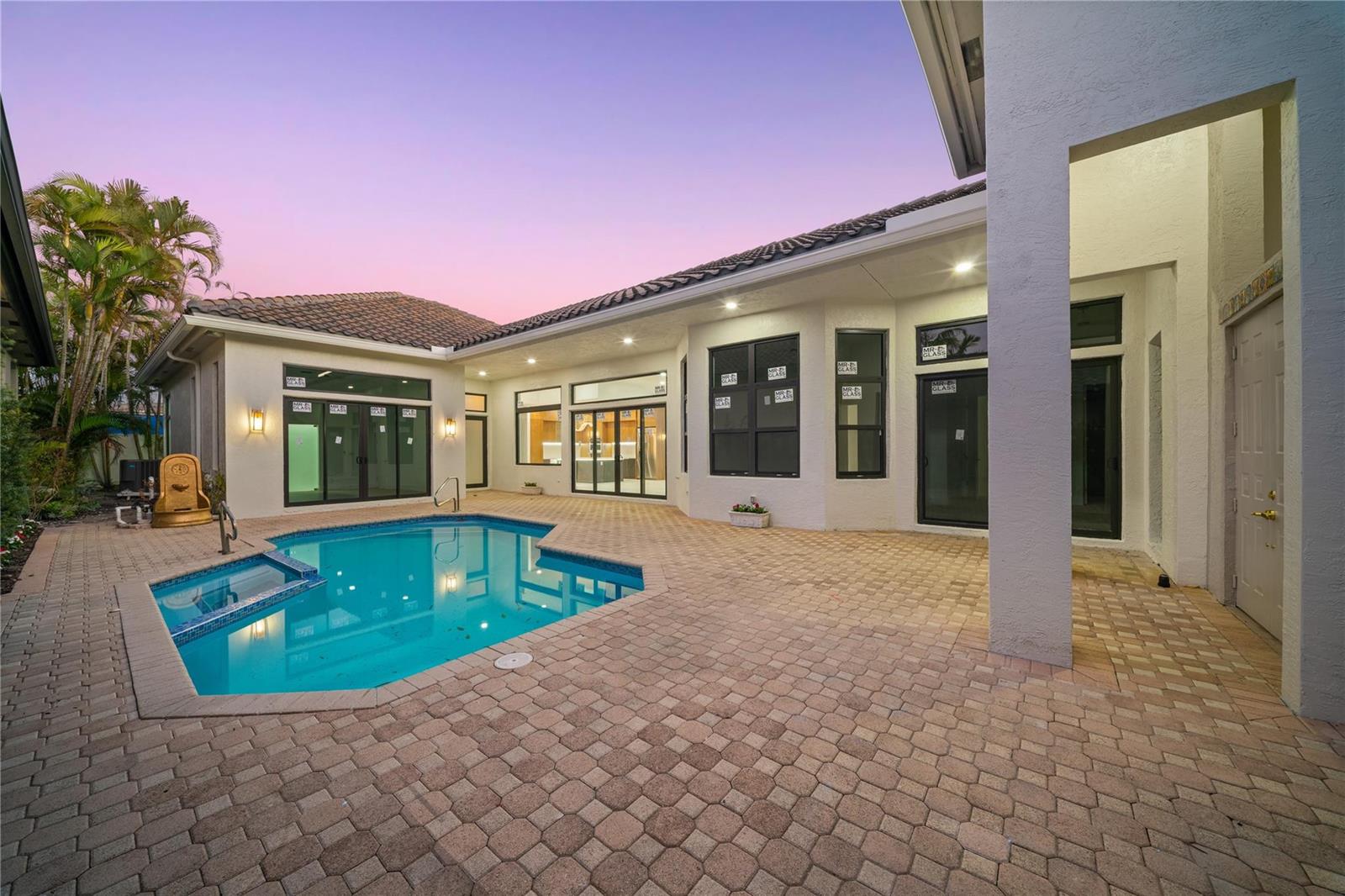 A backyard patio features a swimming pool, stone pavers, and large glass doors at dusk — 22722 El Dorado Drive, Boca Raton FL 33433, BOCA RATON, FL