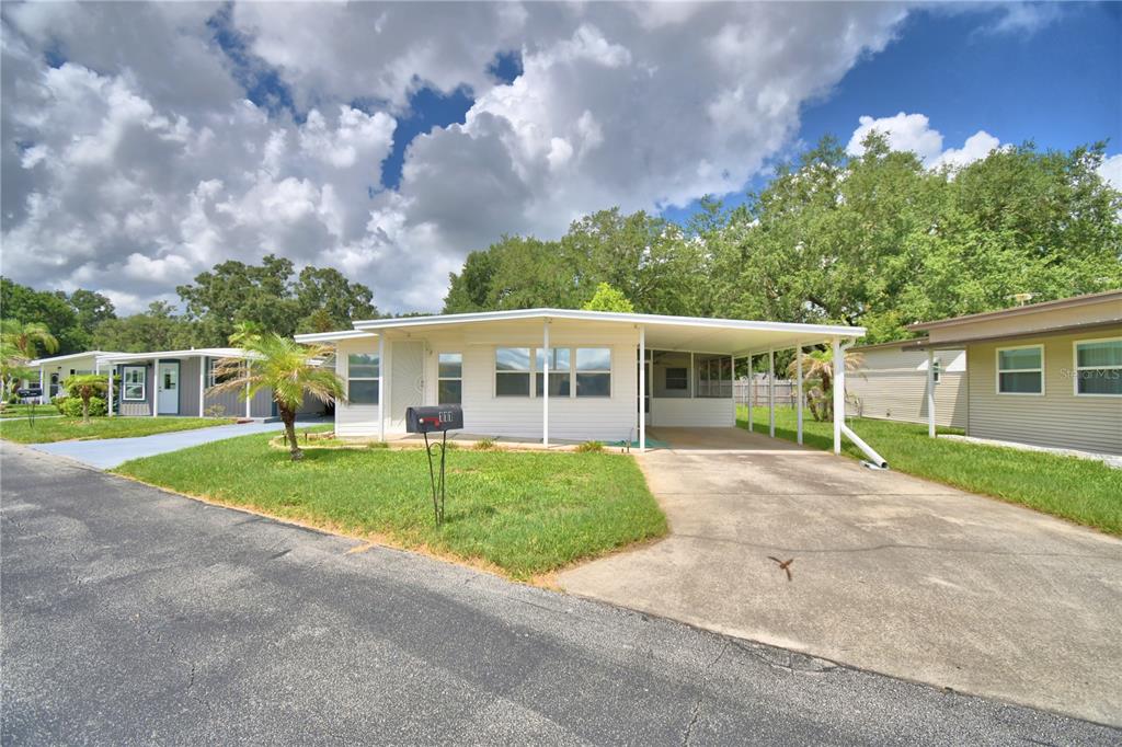 A single-story mobile home with a carport and a front lawn under a cloudy sky — 111 PARADISE LANE, AUBURNDALE, FL