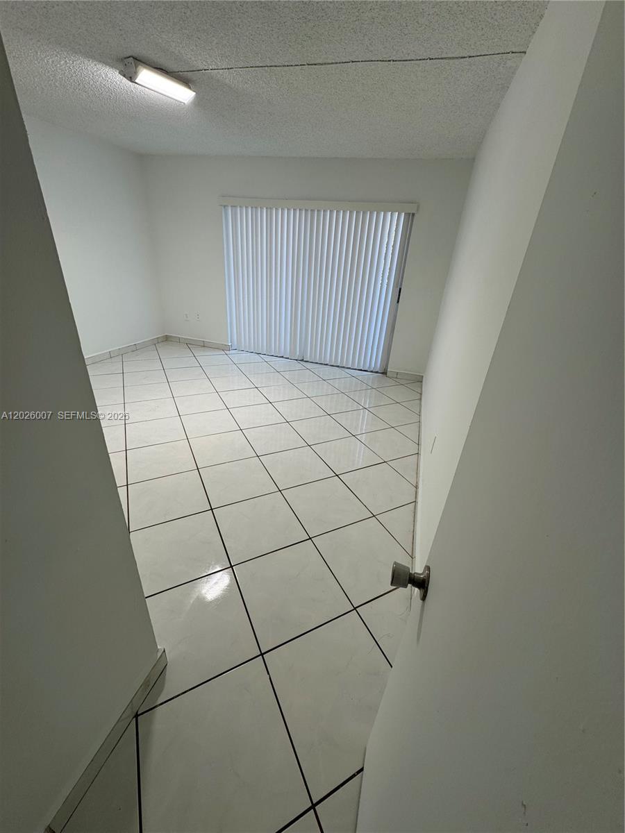 A room with white walls, white tile flooring, and a sliding glass door with blinds — 1555 W 44th Pl # 244, Hialeah FL 33012, HIALEAH, FL