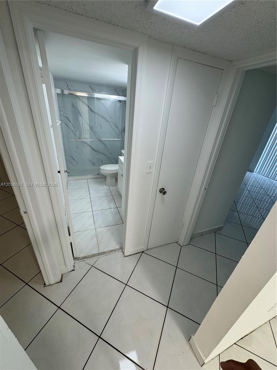 A tiled hallway leads to a bathroom featuring a glass-enclosed shower and white cabinetry — 1555 W 44th Pl # 244, Hialeah FL 33012, HIALEAH, FL