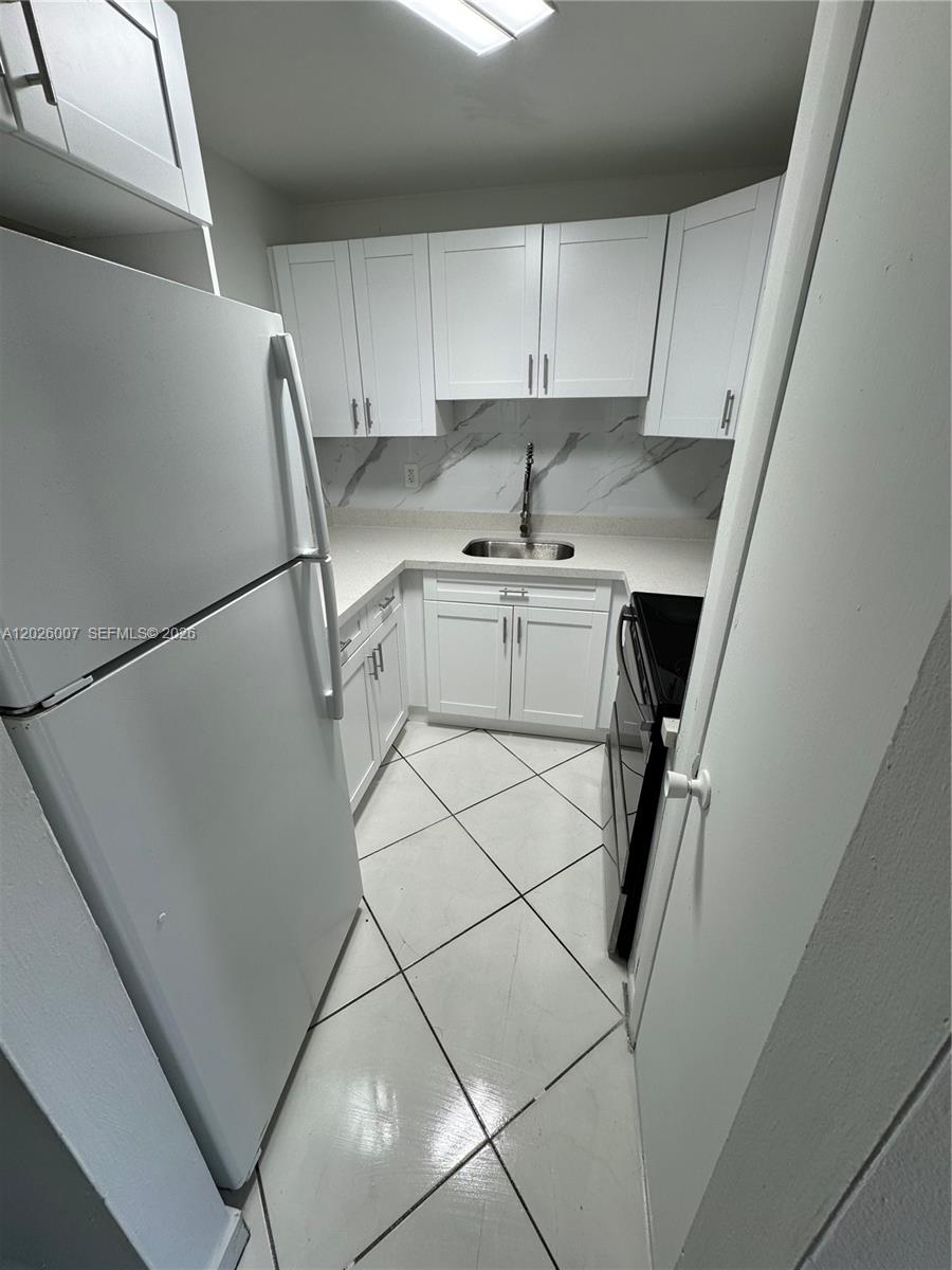 A small kitchen features white cabinets, light countertops, a black stove, and tiled floors — 1555 W 44th Pl # 244, Hialeah FL 33012, HIALEAH, FL