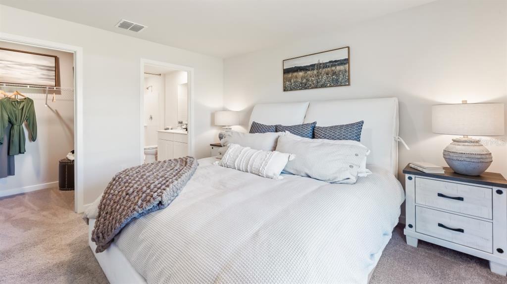 A bedroom features a white upholstered bed, a nightstand with a lamp, and an attached bathroom — 1481 HARMON DRIVE, PORT CHARLOTTE, FL