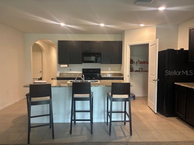 A kitchen features dark cabinets, a granite-topped island with three stools, and tile flooring — 32696 PEZ LANDING LANE, WESLEY CHAPEL, FL