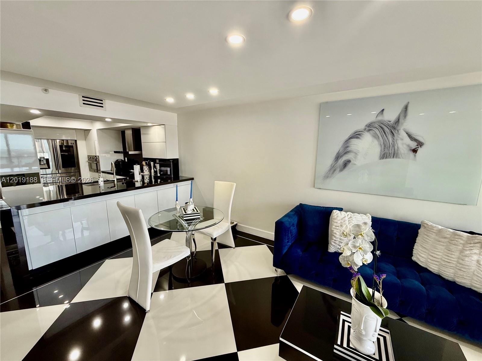 A modern kitchen and living area feature black and white checkered floors and blue seating — 555 NE 15th St # 15H, Miami FL 33132, MIAMI, FL