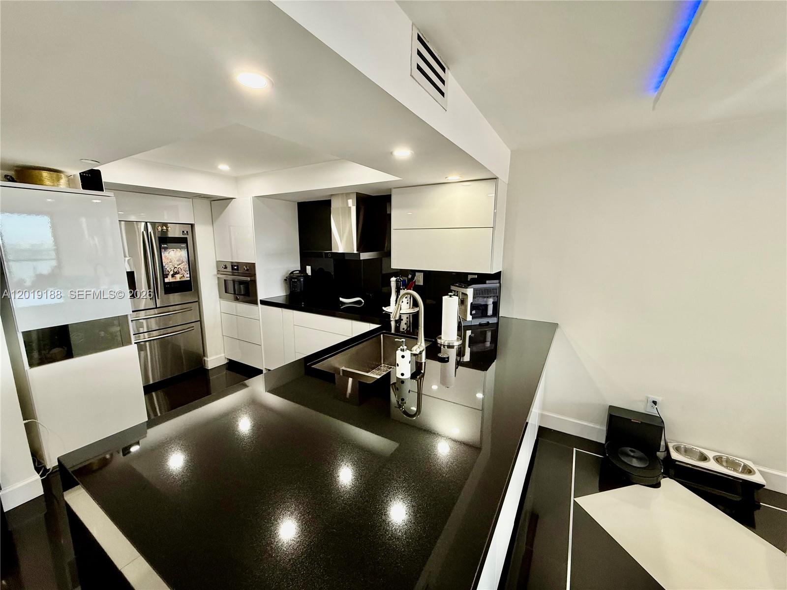 A modern kitchen features black countertops, white cabinetry, stainless steel appliances, and dark flooring — 555 NE 15th St # 15H, Miami FL 33132, MIAMI, FL