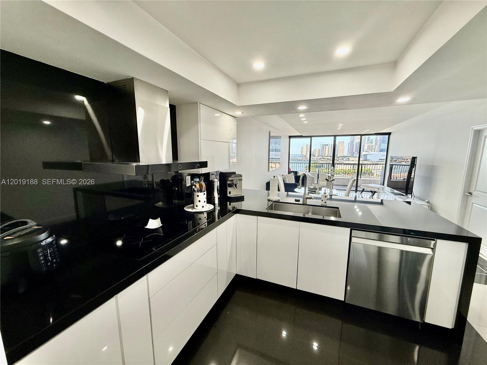 A modern kitchen features white cabinets, black countertops, and a view of the city skyline — 555 NE 15th St # 15H, Miami FL 33132, MIAMI, FL